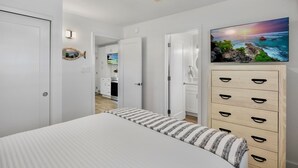 Een slaapkamer met een bed, een kaptafel, een televisie en uitzicht op de keuken.