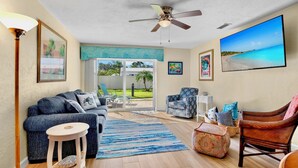 A living room with a blue sofa, a wooden coffee table, a patterned armchair, and a television on the wall. - Jamaica Royale 108 Garden View! (Siesta Key)