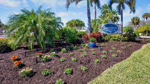 A landscaped area with a sign for 'Jamaica Royale,' surrounded by palm trees and various plants. - Jamaica Royale 108 Garden View! (Siesta Key)