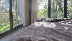 Ein Schlafzimmer mit einem großen Bett, zwei Fenstern mit Vorhängen und Blick auf Grünfläche.