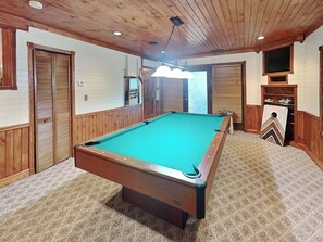 A pool table in a room with wooden paneling and carpeted flooring.