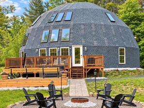 A dome-shaped building with a deck, outdoor seating, and a fire pit.