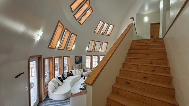 A staircase with wooden steps and a handrail, leading to a landing with a white sofa and a painting. - The Moon House Dome: 10 min away from skiing and golfing. Waterfront. Fishing. (Acra)