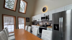 A modern kitchen with white cabinetry, stainless steel appliances, and a dining area with a wooden table and white upholstered chairs. - The Moon House Dome: 10 min away from skiing and golfing. Waterfront. Fishing. (Acra)