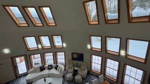 A spacious living room with a large sectional sofa, a coffee table, and multiple seating options. The room features large windows with views of a snowy landscape. - The Moon House Dome: 10 min away from skiing and golfing. Waterfront. Fishing. (Acra)