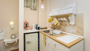 A compact kitchen with a sink, a small refrigerator, a countertop with a cutting board, and a wall-mounted rack with kitchen utensils.