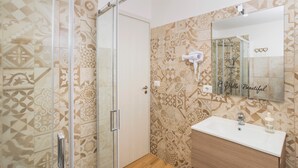 A bathroom with patterned tiles, a glass shower enclosure, a sink with a mirror, and a hairdryer on the wall.