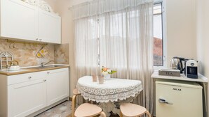 Una cocina compacta con una mesa redonda, dos sillas, un refrigerador y una ventana con cortinas.