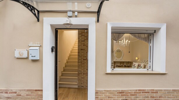 Una escalera conduce a una habitación con ventana, un candelabro y una pequeña mesa con un florero.
