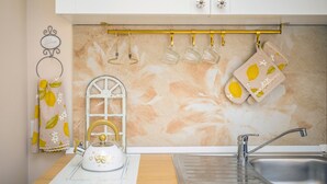 Una cocina con un lavamanos, una tetera, un perchero y un detalle decorativo en la pared.