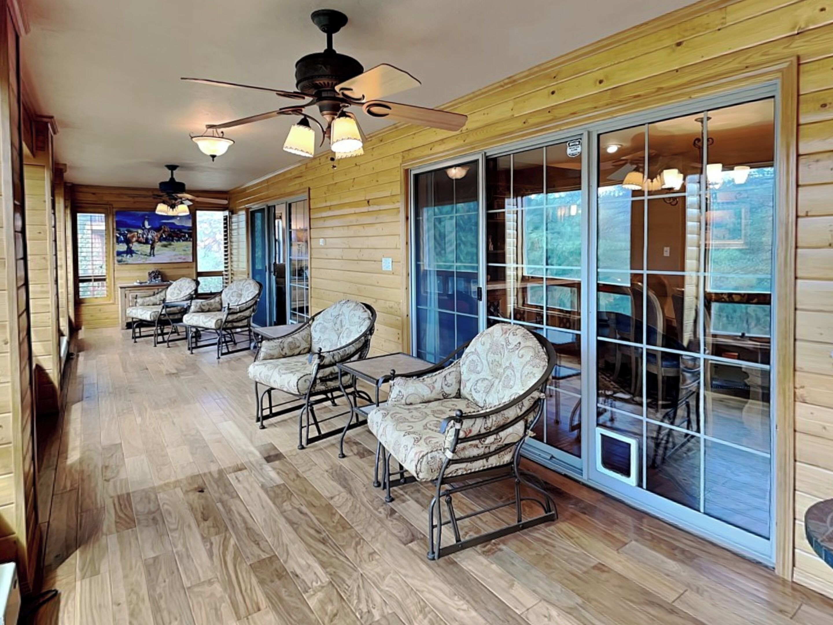 A covered outdoor area with wooden flooring, multiple chairs, and ceiling fans.