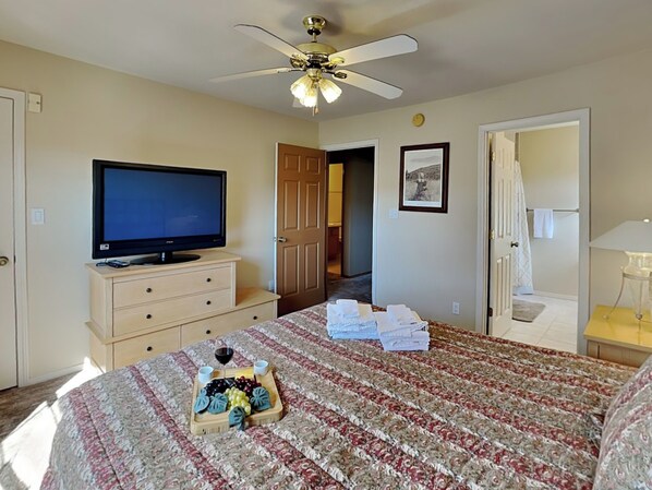 A bedroom with a bed, a TV on a dresser, a ceiling fan, and a door leading to another room. - Sierra Silver by Ruidoso Vacation Rentals (Ruidoso)