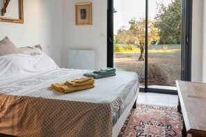 Ein Schlafzimmer mit einem Bett, einer Bank, einem Fenster und Blick ins Freie.