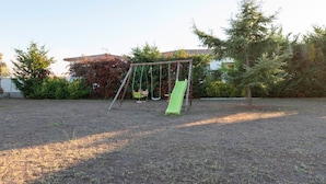 A playground with a swing set and a slide in a grassy area with trees and a building in the background. - Guest Room "Room 2" with Mountain View, Shared Pool and Wi-Fi (Aléria)
