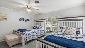 A bedroom with two beds, a ceiling fan, a window with blinds, and a small table.