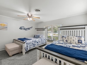 A bedroom with two beds, a ceiling fan, a window with blinds, and a small table.