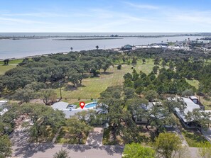 An aerial view of a coastal area with a large body of water, a park with dense trees, and a building with a red marker. - The Sea Glass House by Miss Kitty’s (Rockport)