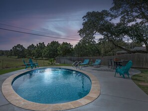 A circular pool with a tiled edge, surrounded by a patio area with chairs and a table. - The Sea Glass House by Miss Kitty’s (Rockport)