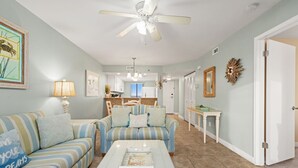 A living room with a striped sofa, a coffee table, and a ceiling fan. - 702 | Cozy Fall Beachfront Retreat—1BR, Gulf Views, Pool & VIP Beach Service (Panama City Beach)