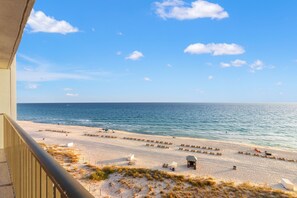 Une vue sur la plage depuis un balcon, avec un ciel dégagé, une plage de sable et l’océan.