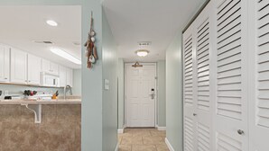 A hallway with a kitchen area on the left, featuring cabinets, a microwave, and a countertop with kitchen utensils. - 702 | Cozy Fall Beachfront Retreat—1BR, Gulf Views, Pool & VIP Beach Service (Panama City Beach)