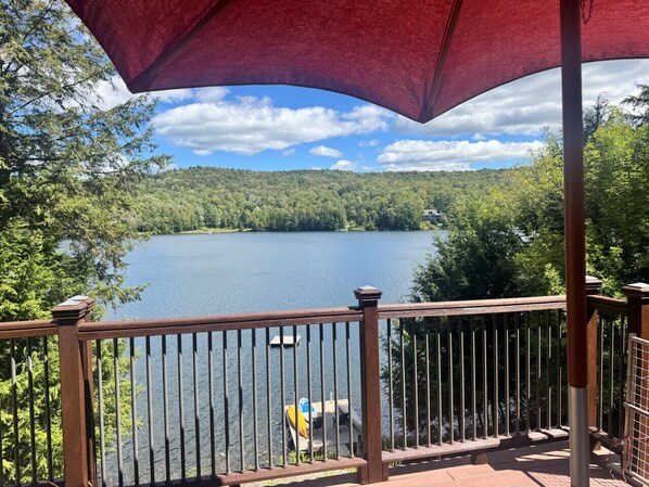 A wooden deck with a railing overlooking a lake, surrounded by trees.