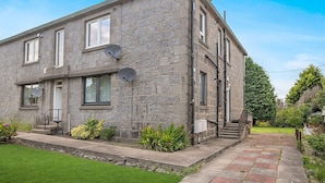 A two-story stone building with satellite dishes, a small garden, and a paved pathway leading to the entrance. - Hilton Road Apartment (Aberdeen)