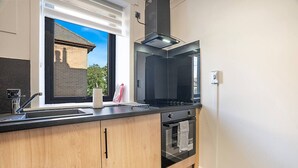 A modern kitchen with a black stove, a built-in oven, and a window overlooking a brick building. - Hilton Road Apartment (Aberdeen)