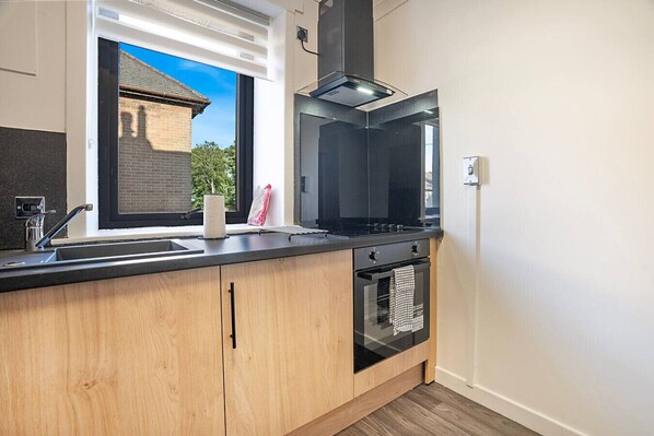A modern kitchen with a black stove, a built-in oven, and a window overlooking a brick building. - Hilton Road Apartment (Aberdeen)