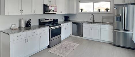 Une cuisine moderne avec des armoires blanches, des appareils en acier inoxydable et un ventilateur de plafond.