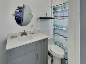 A bathroom with a white sink, a round mirror, a striped shower curtain, and a toilet.