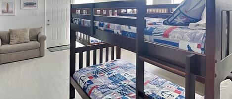 Una cama litera con cubrecama acolchado, un ventilador de techo y una puerta en una habitación con suelo de tonos claros y un sofá.