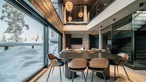 A modern dining area with a large round table and six chairs, a stone accent wall, and a view of a snowy landscape through large windows.