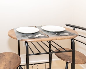 Ein kleiner runder Tisch mit zwei weißen Tellern, schwarzen Metallstühlen und einem schwarzen Metallstuhl mit Rückenlehne.