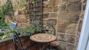 Zona d'estar a l'aire lliure amb dues taules rodones i cadires, envoltada de murs de pedra i una jardiniera de maó amb plantes.