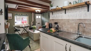 Cuina amb bigues de fusta, zona de menjador amb taula i cadires, màquina de cafè i un rentaplat.