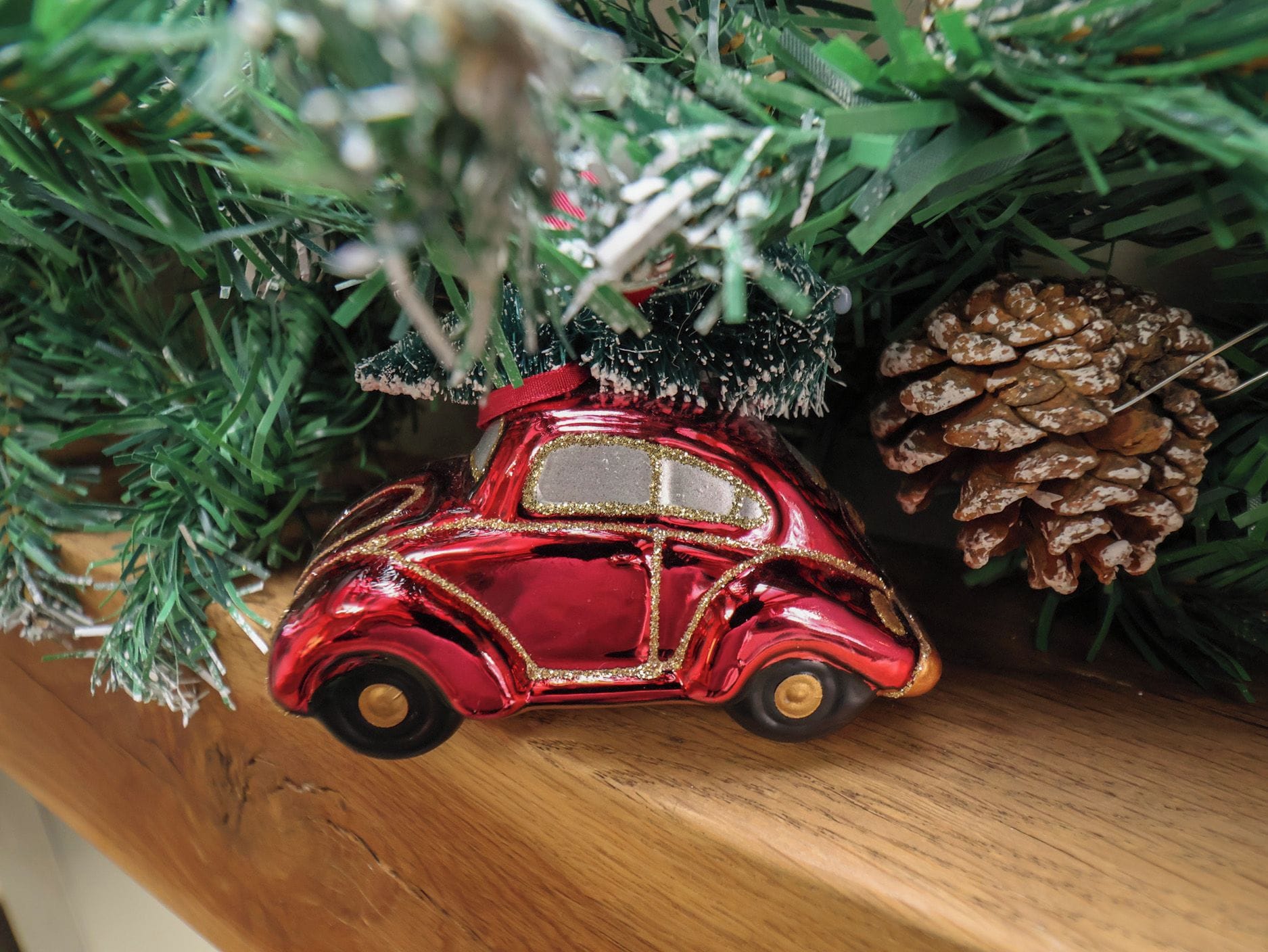 A red ornament shaped like a vintage car hanging on a Christmas tree.