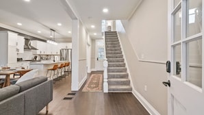 Eine moderne Küche mit weißen Schränken, ein Essbereich mit grauem Sofa und eine Treppe zu einer oberen Ebene.