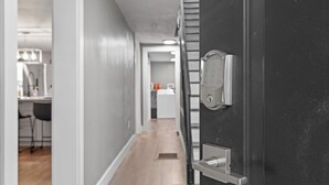 Un pasillo con una puerta moderna, una cocina al fondo y un comedor con sillas.