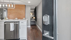 Una cocina moderna con pared de ladrillo decorativa, electrodomésticos de acero inoxidable y una puerta negra con picaporte plateado.