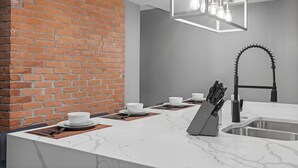 Una cocina moderna con encimera de mármol, pared de ladrillo decorativa e iluminación colgante.