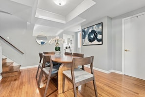 A modern dining area with a wooden table and chairs, a staircase, and a large abstract painting on the wall. - 3BR Shadyside Home | Walk to Walnut | Free Parking (Pittsburgh)