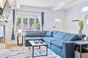 En moderne stue med en hjørnesofa, et sofabord og et stort vindue med gardiner.