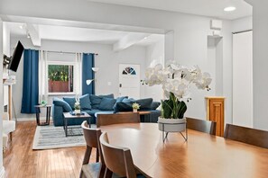 A modern living room with a sofa, a dining table, and a potted orchid. - 3BR Shadyside Home | Walk to Walnut | Free Parking (Pittsburgh)