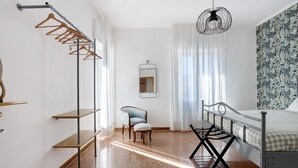 A bedroom with a bed, a chair, a wardrobe with hangers, a mirror, and a patterned wall.
