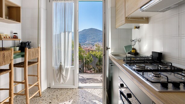 A kitchen with a gas stove, a dining area with a chair, and a view of a mountain through a door.