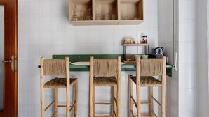 A kitchen with three wooden chairs, a green countertop, and a wooden shelf above holding glassware.