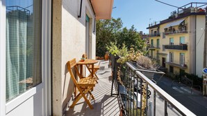 A balcony with a table and chairs, a potted plant, and a view of neighboring buildings.