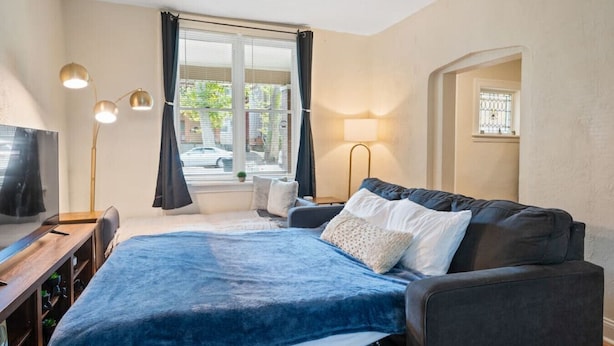 A bedroom with a bed, a desk, a TV, and a window with curtains. - 3 Story home w/ 11 beds! | Close to Pitt & CMU! (Pittsburgh)