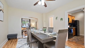 A dining area with a long table, chairs, and a ceiling fan. There is a kitchen visible in the background with wooden cabinets and a black refrigerator. - 3 Story home w/ 11 beds! | Close to Pitt & CMU! (Pittsburgh)